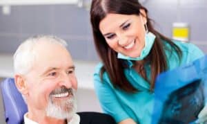 Smiling dentist with patient in dental office discussing implant denture options.