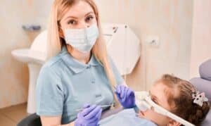 Pediatric dentist in Houston wearing protective mask and gloves examining young patient's teeth.