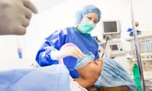 Dentist in surgical attire preparing sedation mask for patient during dental implant procedure in Houston.
