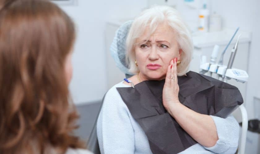 Patient experiencing jaw pain during dental implant recovery consultation with dentist.