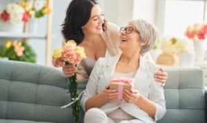 Adult daughter gifting flowers and present to smiling mother on Mother's Day celebration.