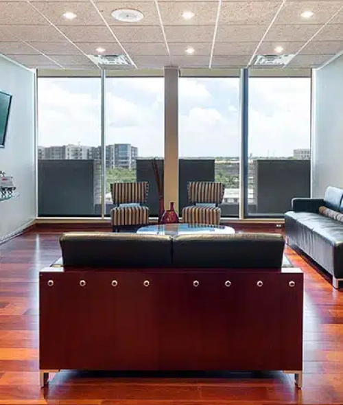Modern dental office reception area with burgundy desk, leather chairs, and floor-to-ceiling windows overlooking city skyline.
