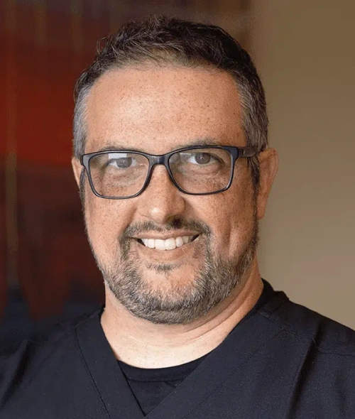 Man wearing glasses smiling at camera in professional portrait setting for dental practice.