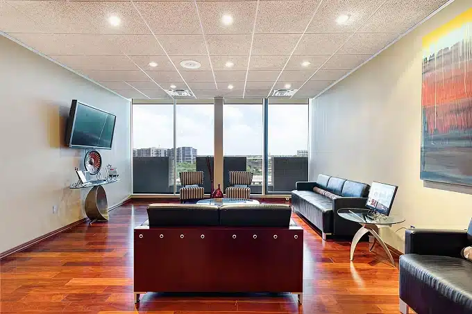 Modern dental office reception area with burgundy desk, wooden flooring, and city skyline views through windows.